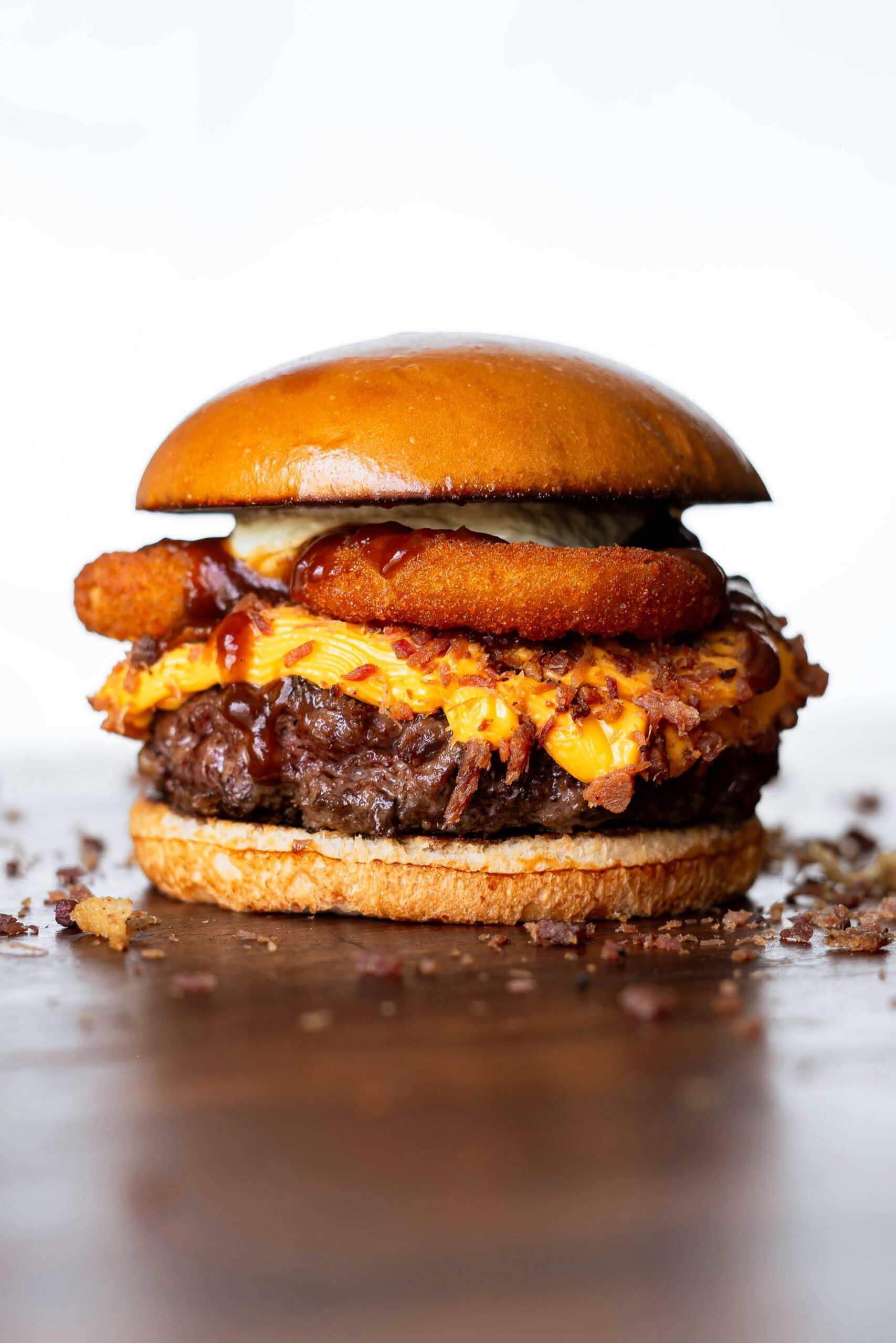 Delicious cheeseburger topped with onion rings and BBQ sauce on a wooden surface.