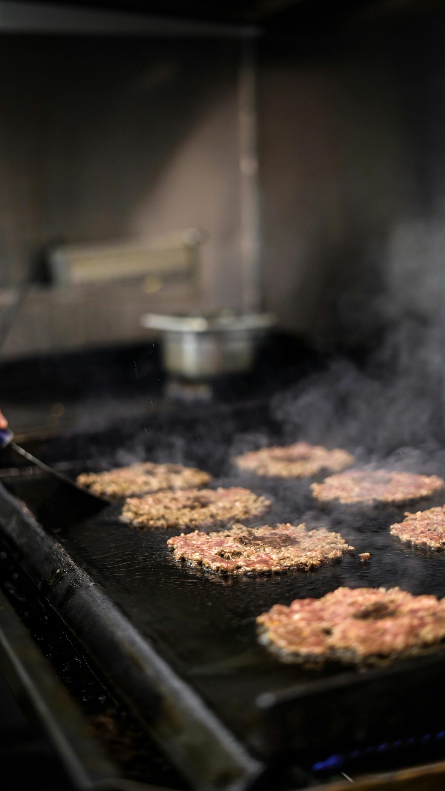 Close-up of sizzling burger patties grilling on a commercial kitchen surface.